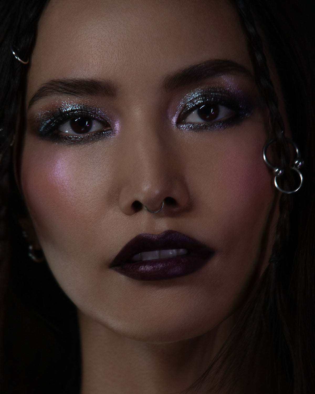 Close-up of a person with dramatic makeup and earrings against a dark background